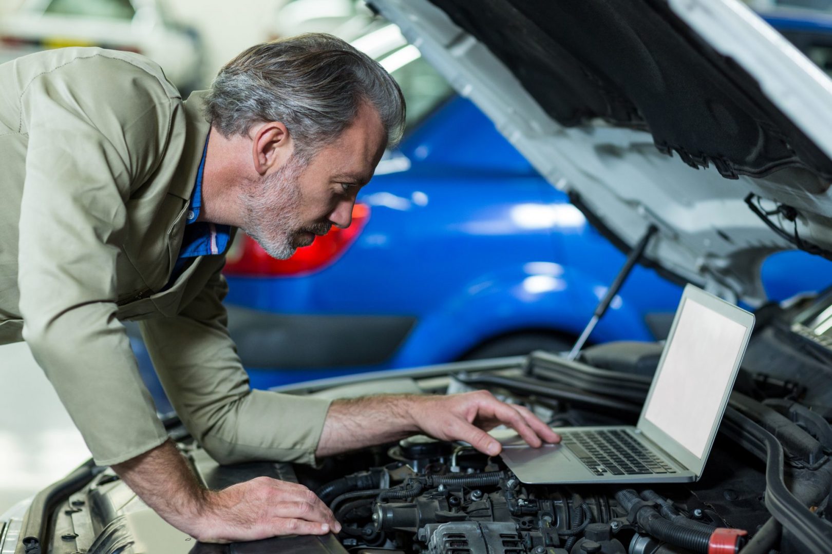 Mécanicien utilisant un ordinateur portable lors de l'entretien d'un moteur de voiture dans un garage de réparation